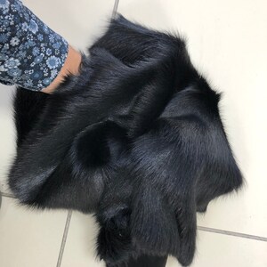 May include: A black fur pelt, folded and displayed on a white tiled surface.