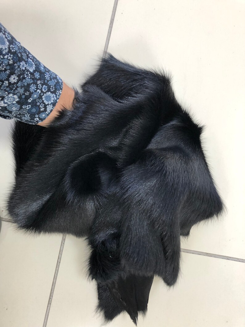 May include: A black fur pelt, folded and displayed on a white tiled surface.