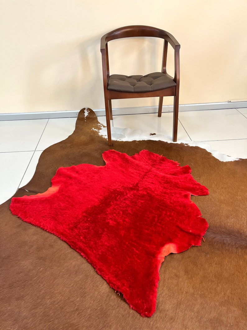 Peut inclure: Un tapis en fausse fourrure rouge sur un tapis en peau de vache brune et blanche. Une chaise en bois avec un si&egrave;ge en cuir brun est &agrave; l'arri&egrave;re-plan.