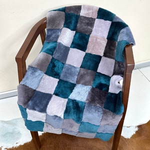 May include: A patchwork throw blanket with squares of teal, gray, and light gray faux fur. The blanket is draped over a wooden chair.
