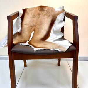 Op de afbeelding: Een bruine houten stoel met een bruine leren zitting en een bruin en wit dierenhuidkleed dat over de rugleuning en de zitting is gelegd.