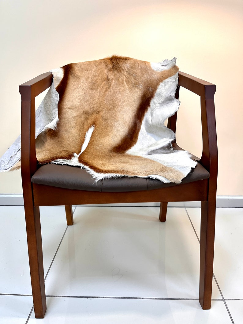 Op de afbeelding: Een bruine houten stoel met een bruine leren zitting en een bruin en wit dierenhuidkleed dat over de rugleuning en de zitting is gelegd.