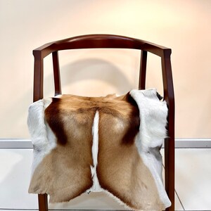May include: A brown wooden chair with a curved back and a white and brown animal skin rug draped over the seat.