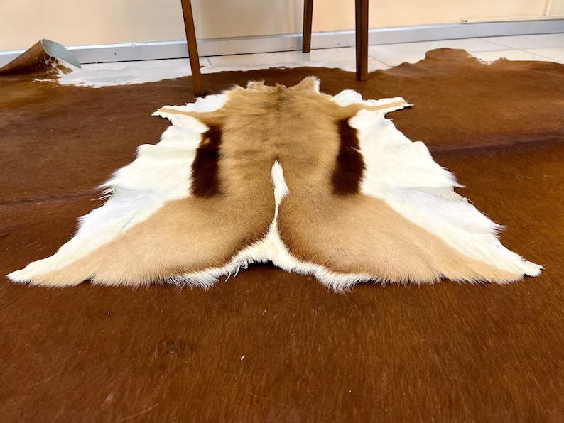 May include: A brown, white, and black animal hide rug. The rug is made of fur and has a natural, rustic look.