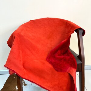 Peut inclure: Une peau de daim rouge avec un dessous doux et duveteux. La peau est drap&eacute; sur une chaise en bois.