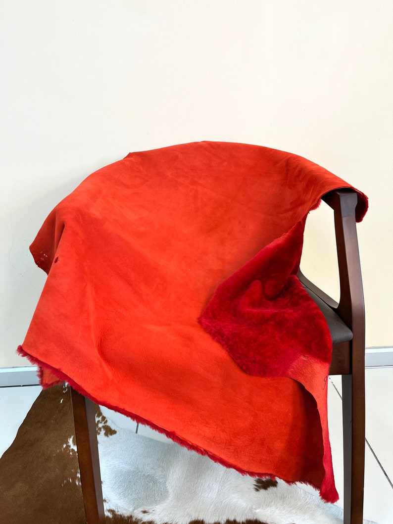 Peut inclure: Une peau de daim rouge avec un dessous doux et duveteux. La peau est drap&eacute; sur une chaise en bois.