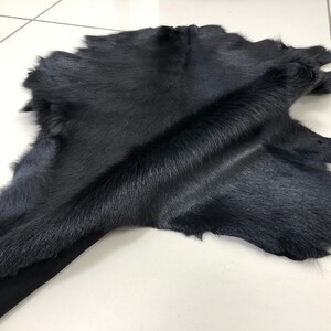 May include: A black cowhide rug with a soft, short fur. The hide is folded in the middle, showing the texture of the fur.
