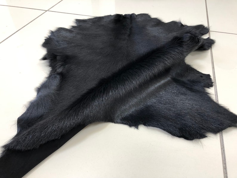 May include: A black cowhide rug with a soft, short fur. The hide is folded in the middle, showing the texture of the fur.