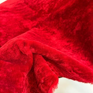 Peut inclure: Gros plan sur un tissu de velours rouge vif avec une texture douce et duveteuse. Le tissu est pli&eacute; et drap&eacute;, r&eacute;v&eacute;lant son toucher luxueux.