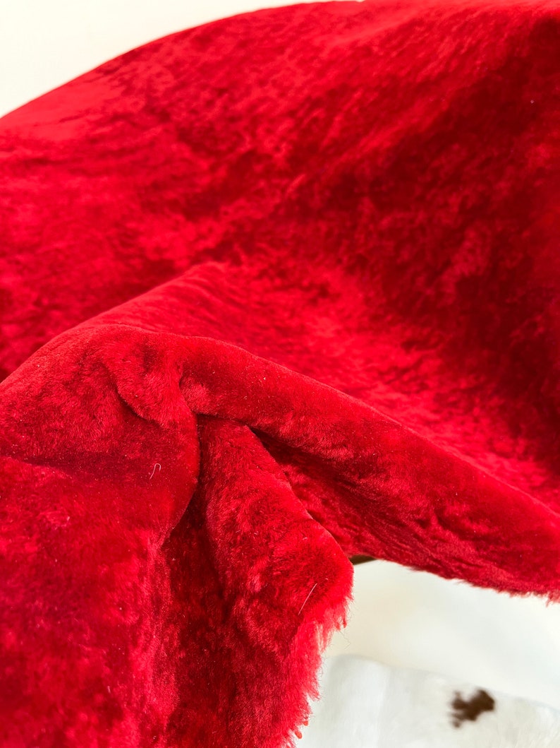 Peut inclure: Gros plan sur un tissu de velours rouge vif avec une texture douce et duveteuse. Le tissu est pli&eacute; et drap&eacute;, r&eacute;v&eacute;lant son toucher luxueux.