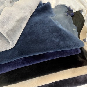 May include: A stack of different colored sheepskin hides in shades of blue, black, and beige. The hides are arranged in a pile, with the blue hides on top.