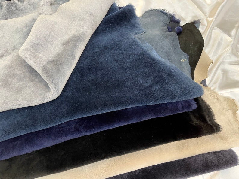 May include: A stack of different colored sheepskin hides in shades of blue, black, and beige. The hides are arranged in a pile, with the blue hides on top.