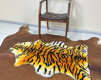 Puede incluir: Una alfombra de piel de vaca marrón y blanca con una alfombra de piel sintética de tigre encima. La alfombra de piel de tigre es naranja, negra y blanca.