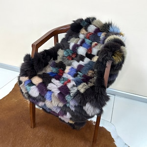 May include: A colourful patchwork fur throw with a mix of brown, black, white, blue, purple and red fur pieces. The throw is draped over a wooden chair.