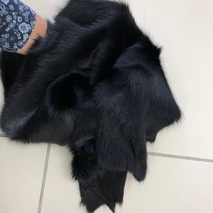 May include: A black fur pelt with a soft, plush texture. The fur is thick and dense, and the pelt is folded in half.