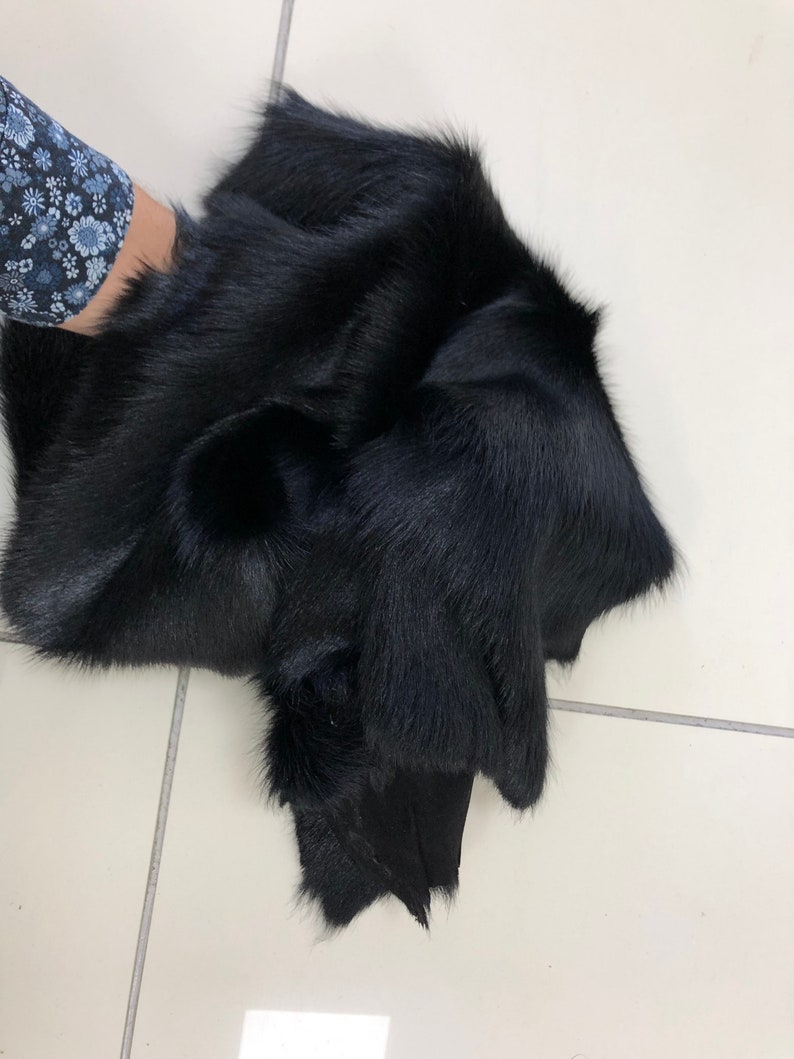 May include: A black fur pelt with a soft, plush texture. The fur is thick and dense, and the pelt is folded in half.