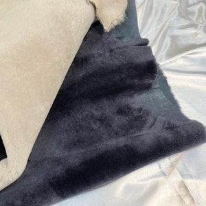 May include: Two pieces of faux fur fabric, one white and one dark gray, are folded and laid out on a white surface.