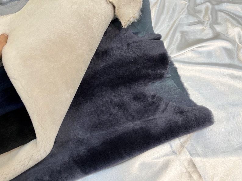 May include: Two pieces of faux fur fabric, one white and one dark gray, are folded and laid out on a white surface.