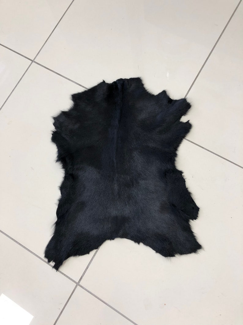 May include: A black cowhide rug with a natural, slightly textured surface.