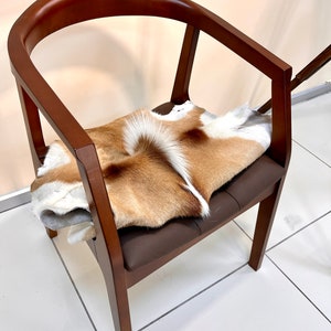 Op de afbeelding: Een houten stoel met een bruine leren zitting en een bruin en wit dierenvel dat op de zitting is gelegd.