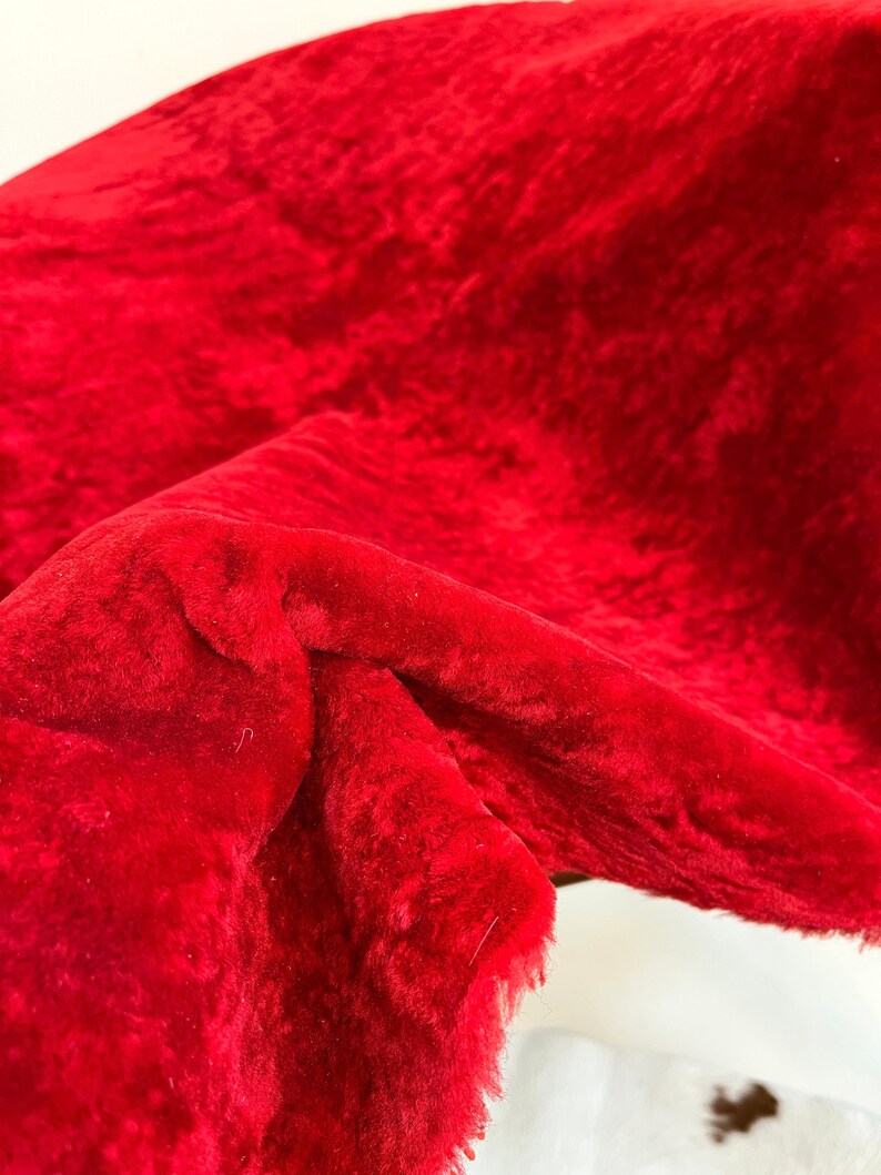 Peut inclure: Gros plan sur un tissu rouge duveteux avec une texture douce et moelleuse. Le tissu est pli&eacute; et drap&eacute;, montrant la texture et la couleur.