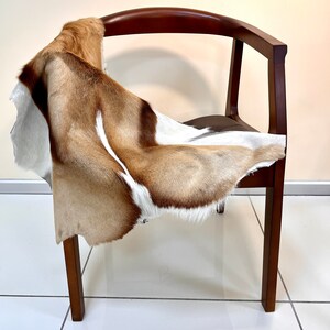 May include: A brown and white animal hide draped over a wooden chair with a curved back.