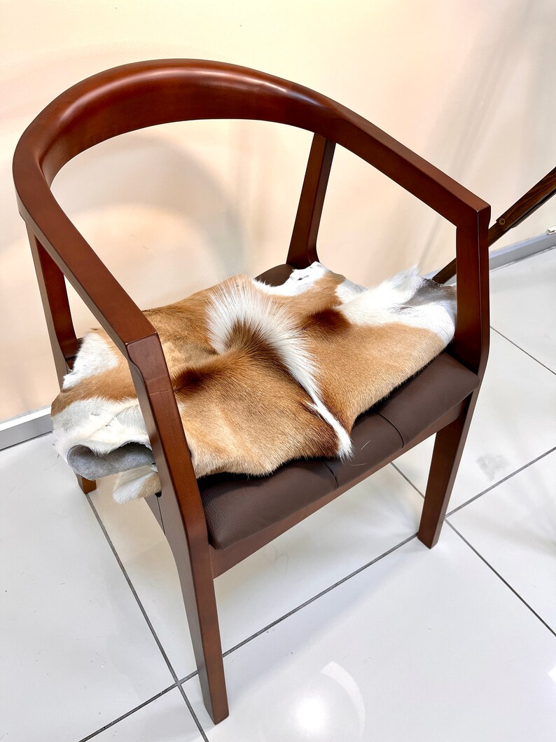 May include: A wooden chair with a brown leather seat and a brown and white animal skin placed on top of the seat.