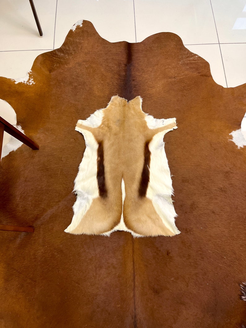 May include: A brown cowhide rug with a smaller, light brown antelope hide rug in the center. The antelope hide has a distinctive pattern of dark brown stripes.