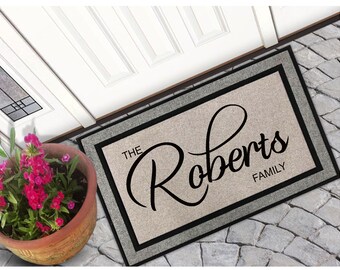 May include: A beige doormat with a black border and the text "The Roberts Family" in a black cursive font.