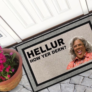 May include: Rectangular doormat with a beige background and a black border. The mat features the text "HELLUR HOW YER DERN?" in bold black letters and an image of a smiling woman.