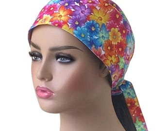May include: A colorful floral print surgical scrub hat with a tie at the back. The hat is white with a variety of flowers in shades of pink, purple, yellow, orange, and blue.