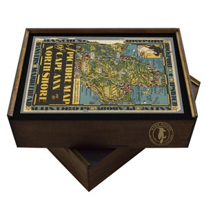 May include: A wooden box with a vintage picture map of Cape Ann and the North Shore. The map is in shades of blue, green, and yellow. The box has a black felt lining and a brown wooden lid. The lid has a circular sticker with a penguin logo and the text "WW PUZZLES".