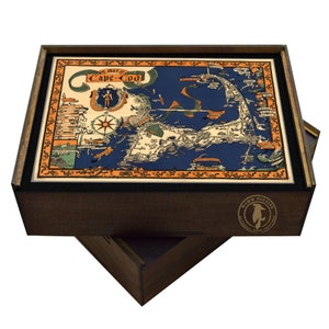 May include: A wooden box puzzle featuring a vintage map of Cape Cod. The box is brown with a black interior and a black and white logo on the bottom. The map is in shades of blue, orange, and green.