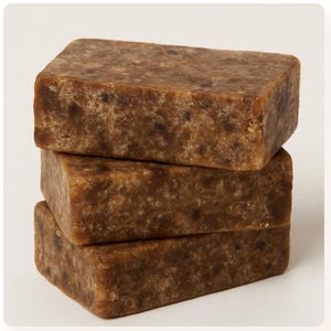 Peut inclure: Trois barres rectangulaires de savon brun foncé empilées. Le savon a une surface texturée avec des mouchetures plus foncées. Les barres sont bien disposées, montrant leur forme et leur couleur sur fond blanc.
