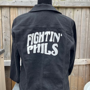 Peut inclure: Veste en jean noire avec l'inscription "Fightin' Phils" en blanc sur le dos.