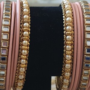 May include: A set of pink and gold bangles with mirrored accents and pearl embellishments.