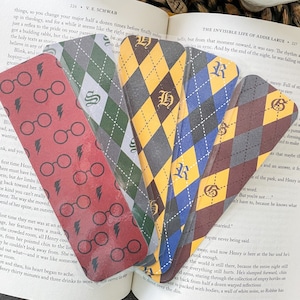 May include: A set of six bookmarks featuring a Harry Potter theme. The bookmarks are made of cardstock and feature a checkered pattern in the Hogwarts house colors. Each bookmark has a different house crest and letter. The bookmarks are arranged in a fan shape.