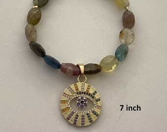 May include: A 7 inch bracelet with a gold clasp and a colorful evil eye charm. The bracelet is made of various semi-precious stones in shades of green, brown, blue, and yellow.