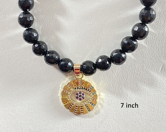 May include: Black onyx beaded bracelet with a gold evil eye charm. The bracelet is 7 inches long.