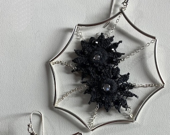 May include: A pair of silver earrings with black lace flowers and rhinestones, set in a web-like design. The earrings are 2.5 inches in diameter.