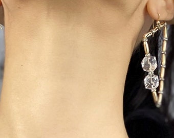 May include: A pair of earrings with gold hoops and clear crystal accents. The larger earring has three crystal beads and the smaller earring has one crystal bead.