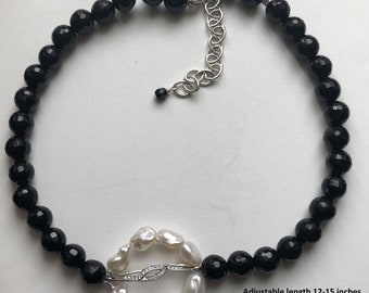 May include: Black onyx bead necklace with a white freshwater pearl pendant. The pendant is a circle with a silver clasp and a small diamond. The necklace is adjustable from 12-15 inches long. Pendant is 1.5 x 1 inches. 6mm beads.