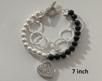 May include: A silver bracelet with black and white beads, a heart charm with a lightning bolt design, and a toggle clasp. The bracelet is 7 inches long.