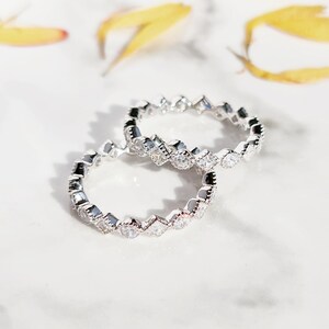 May include: Two silver rings with a row of small, clear, square-shaped stones set in a scalloped design.