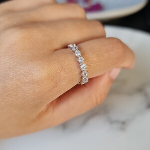 May include: A silver ring featuring a row of small, round, clear stones set in a delicate, scalloped design.