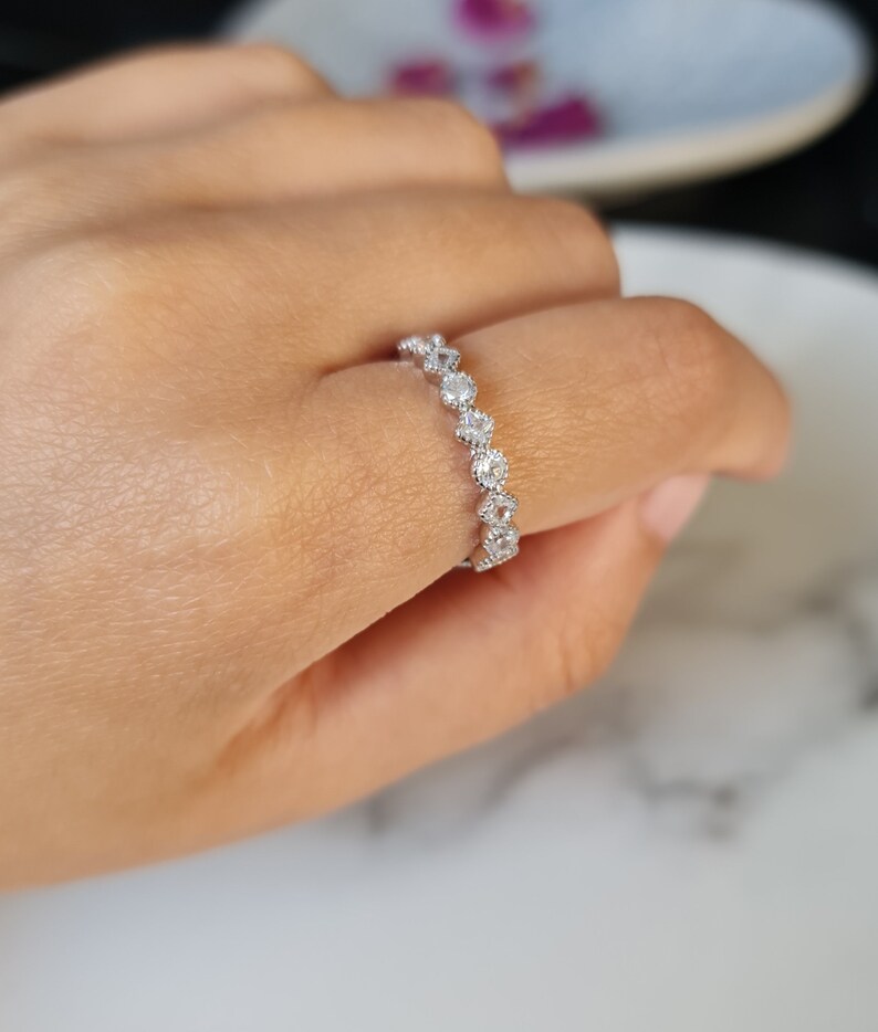 May include: A silver ring featuring a row of small, round, clear stones set in a delicate, scalloped design.