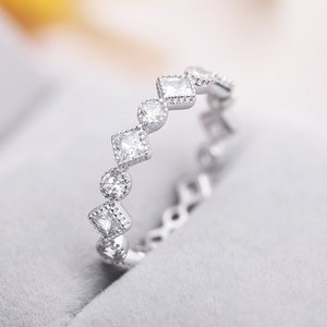 May include: A silver ring featuring a row of small, clear, square-shaped stones set in a delicate, scalloped design.