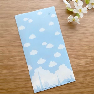 May include: A light blue plastic folder with a white aeroplane, clouds, and a cityscape silhouette. The folder has a dotted line along the bottom edge.