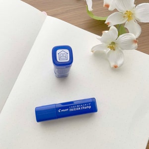 May include: A blue and white Pilot FriXion Stamp with the text "こすると消えるスタンプ FRIXION STAMP" on the side. The stamp features a house icon with a laptop inside.