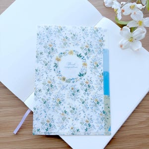 May include: A white notebook with a floral patterned plastic pocket folder. The folder has a blue and white tabbed divider with the text "Floral composition" in a circle.